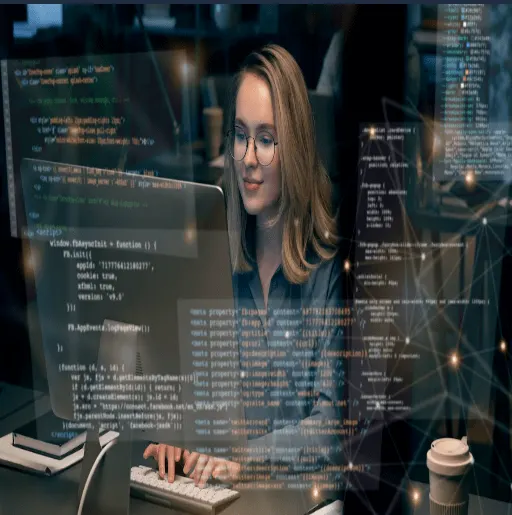 A young woman with glasses and a focused expression is working on a computer in a dimly lit office. Holographic-style programming code and digital elements overlay the image, symbolizing advanced technology and software development. A coffee cup is placed on the desk beside her.